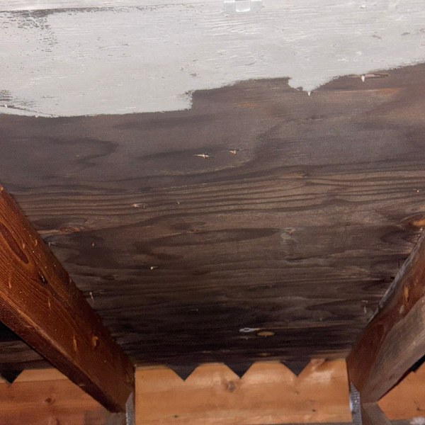 Roof sheathing seen from inside an attic, with a large dark water stain spreading across the boards below a clean unstained section